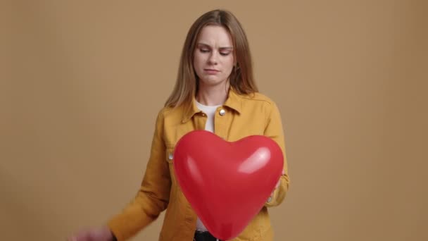 若い女性は 心臓の形をした風船を保持し 動揺している 暗い女の子のクローズアップショット愛のシンボルをぽんと鳴らす 高品質4K映像 — ストック動画