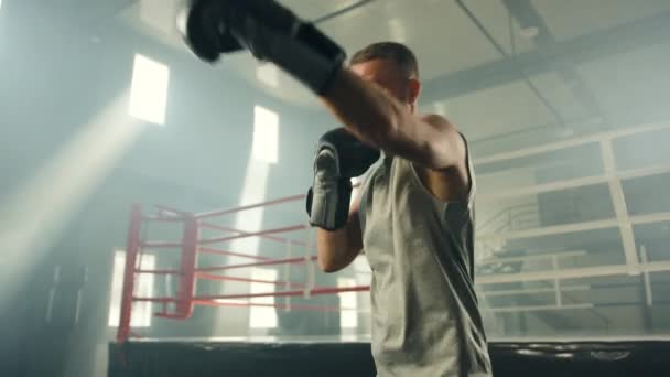 ボクシングリングの近くに立ってジムで影のボクシングを実行するボクシング手袋で中年のボクサーの中ショット 男は空気中でパンチをスローします 高品質4K映像 — ストック動画