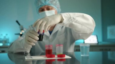Veteriner kliniğindeki laboratuvarda analizlerle konteynırları kapatan orta yaşlı bir erkek doktor resmi. Adam laboratuvar önlüğü, tıbbi eldiven, maske ve şapka giyiyor. Yüksek kalite 4k görüntü