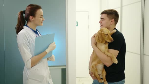 照片上有两只公猎狗的主人和年轻的女兽医站在诊所里说话 男人手里拿着宠物 医生手里拿着文件夹 高质量的4K镜头 — 图库视频影像