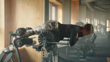 Tam teçhizatlı spor salonunda sağlıklı genç kadın kalçalı jambon geliştiricisi üzerinde egzersiz yapıyor. Kadın kalça ve sırt uzantısını yatay olarak yapıyor ve kollarını göğsüne kavuşturuyor. Yüksek kalite 4k görüntü