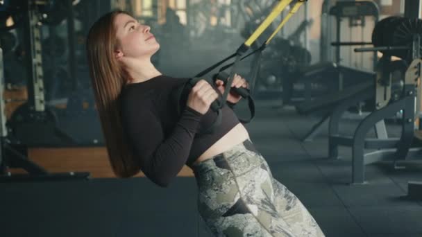 采用悬挂式训练装置拍摄的长发年轻的运动可爱女子的侧面照片 女人在设备齐全的体育馆里锻炼 高质量的4K镜头 — 图库视频影像