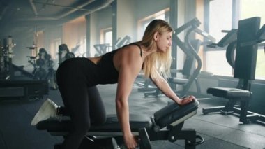 Oldukça atletik bir sarışın, iyi donanımlı spor salonunda halterli bir bankta egzersiz yapıyor. Kadın, tek kollu dambıl gibi sıralanmış, dar siyah elbiseler giyiyor. Yüksek kalite 4k görüntü