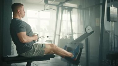 Formda bir adamın kablolu yayın makinesinde kablo yayını yaparken profil fotoğrafı. Sporcu bankta oturur ve kolu karnının altına doğru çeker. Yüksek kalite 4k görüntü