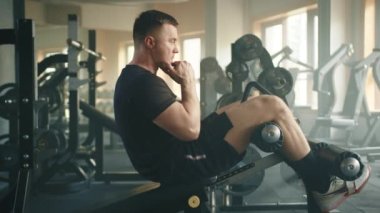 Genç bir adamın iniş bankında mekik çekerken çekilmiş profil fotoğrafı. Sporcu göğsünü kalça hizasına getirmek için gövdesini kaldırır ve başlangıç pozisyonuna geri döner. Yüksek kalite 4k görüntü