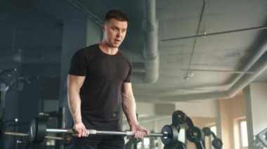 İyi donanımlı spor salonunda halterle egzersiz yapan zinde bir genç. Sporcu hafif halteri kaldırır ve kollarını düz tutar. Yüksek kalite 4k görüntü