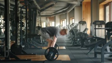 Kaslı vücutlu bir sporcunun halter kaldırma hareketi. Sporcu halteri yerden uyluk seviyesine kaldırır ve aşağı indirir. Yüksek kalite 4k görüntü