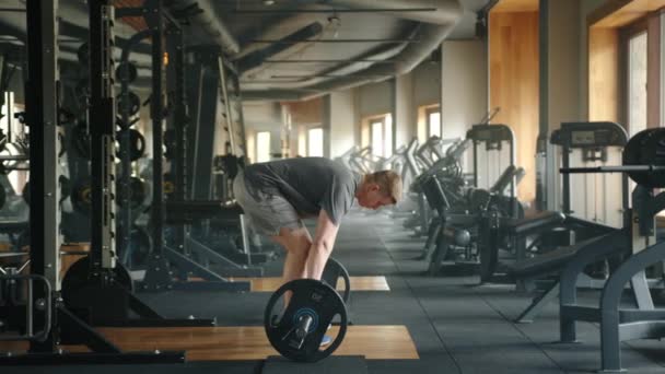 筋肉体のアスリートのプロフィールショットは バーベルのデッドリフトを実行します スポーツマンは 床から太ももレベルまでの鐘を持ち上げ それを下げる 高品質4K映像 — ストック動画