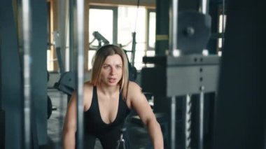 Güzel sarışın ve fit vücutlu, kablolu TV makinesinde egzersiz yapma süreci. Kadın öne eğiliyor ve ağırlığı göğsüne doğru itiyor ve geriye doğru iniyor. Yüksek kalite 4k görüntü