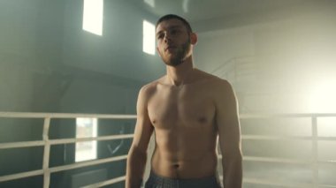 Çıplak gövdeli genç yakışıklı boksör dövüşe hazırlanıyor, ringde boyun kaslarını geriyor. Sporcu yumruklarını kapar, dövüşmeye hazır olduğunu gösterir. Yüksek kalite 4k görüntü