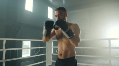 Orta yaşlı boks eldivenli bir sporcu gölge boksu antrenmanı yapıyor. Çıplak ve formda bir boksör spor salonunda ringe yumruklar atıyor. Yüksek kalite 4k görüntü