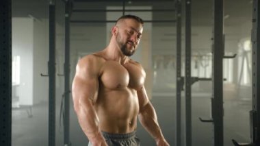 Orta yaşlı vücut geliştirici gülümseyen, göğsünde kollarını kavuşturan çıplak bir vücut geliştirme resmi. Adam ferah bir spor salonunda güçlü ekipmanlarıyla duruyor. Yüksek kalite 4k görüntü