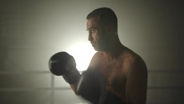 ジムで影のボクシングを行う中年のボクサーの中プロファイルショット ボクシンググローブのスポーツマンは空気中でパンチをスローします 謎の背景 高品質4K映像 — ストック動画