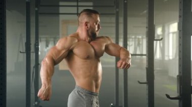 Orta yaşlı sporcunun, kaslı gövdesini, pazılarını ve pazılarını gösteren profil fotoğrafı. Adam jimnastik salonunda güç rafının arkasında duruyor. Yüksek kalite 4k görüntü