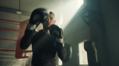 Genç formda boksör boks eldiveni giyerek gölge boksu egzersizleri yapıyor. Sporcu havaya yumruklar atıyor. Spor salonunda boks ringiyle antrenman yapan bir adam. Yüksek kalite 4k görüntü
