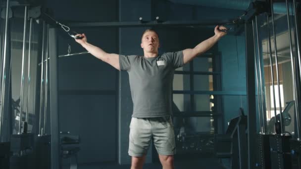 若い陸上競技の男はケーブルクロスオーバーマシンで演習を行う スポーツマンは 頭に手をカール ケーブルクロスオーバーの間に立ってカール二足を実行します 高品質4K映像 — ストック動画
