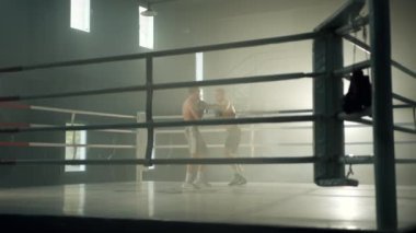 Boks eldivenli çıplak vücutlu iki boksör, spor salonunda boks ringinde dövüşüyor. Rakipler birbirlerine yumruk atıyor. Puslu bir arkaplan. Yüksek kalite 4k görüntü