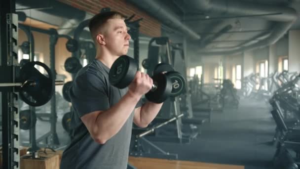 年轻运动员站在体育馆里进行二头肌卷曲的过程 男人们在宽敞的健身房里锻炼 有大量的力量训练设备 高质量的4K镜头 — 图库视频影像