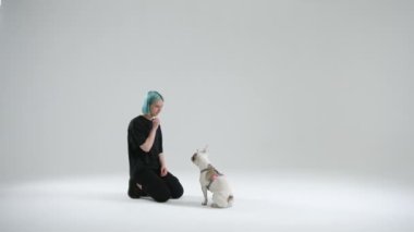 Genç bayan usta, Fransız bulldog 'una ismine cevap vermeyi öğretiyor. Kadın, köpeğin gözlerine bakması için çenesinin yanında yemek tutuyor. Ödül olarak yiyecek. Yüksek kalite 4k görüntü