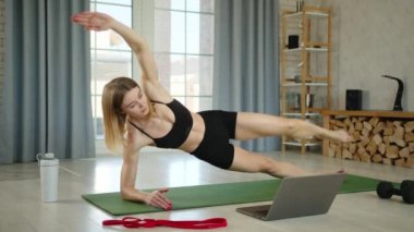 Genç fitness eğitmeni evde online antrenman yapıyor. Basın için alıştırmalar. Kadın antrenör yan yatmış, bacağını çekmiş, dizinin üstüne çökmüş. Yüksek kalite 4k görüntü
