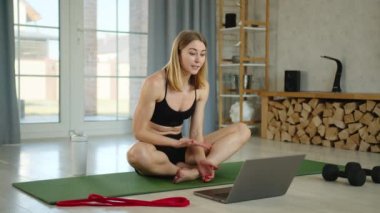 Yakışıklı genç sarışın, defter kullanarak evde fitness antrenmanı yapıyor. Kadın bir paspasın üzerine oturup nefes egzersizlerinin nasıl yapıldığını anlatıyor. Yüksek kalite 4k görüntü