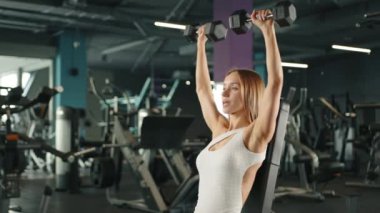 Genç atletik kadın spor salonunda omuz presi yapıyor. Beyaz giysiler içinde. Yüksek kalite 4K görüntü. yavaş çekim 