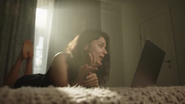 Μπρουνέτ Επικοινωνεί Μέσω Βιντεοκλήσης Στο Λάπτοπ Ξαπλωμένη Μπρούμυτα Στο Κρεβάτι — Αρχείο Βίντεο