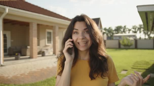 Улыбающаяся Красивая Юная Брюнетка Говорящая Мобильному Телефону Прогуливаясь Двору Солнечный — стоковое видео