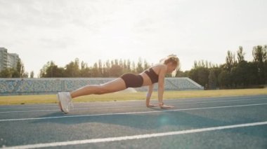 Stadyumda koşu pistinde egzersiz yapan formda bir kadının profil fotoğrafı. Zayıf sarışın temiz havada şınav çekiyor. Koşmadan önce ısınıyorum. Doğa. Yüksek kalite 4k görüntü