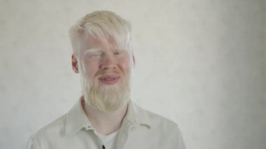 Orta derecede gülümseyen albino adamın kameraya doğru bakması. Geniş bir gülümseme. Beyaz tişörtlü, fevkalade bir adam, hayattan zevk alıyor. Beyaz arka plan. Yüksek kalite 4k görüntü