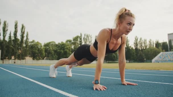 适合年轻的金发姑娘在露天体育场做俯卧撑 漂亮的女人在跑出去之前正在热身 健康的生活方式 高质量的4K镜头 — 图库视频影像