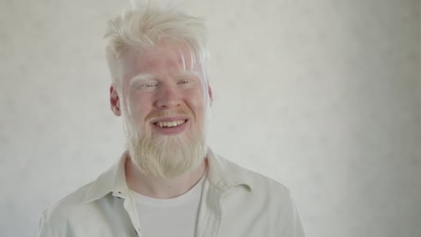 白い背景に白い服を着て アルビニズムと若い笑い髭の男の肖像画 アルビノの中間体を閉じる 珍しい外見の男 高品質4K映像 — ストック動画