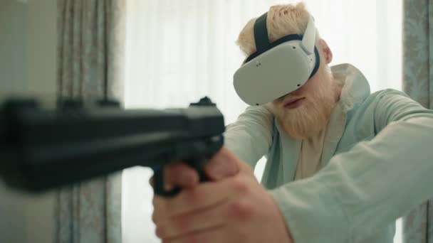 大黒のおもちゃ銃で仮想現実のメガネでアルビノ男の中密室 自宅でデジタル世界でシューティングゲームをプレイするアルビニズムを持つ髭の男 高品質4K映像 — ストック動画