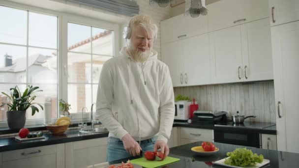 Mooie Lange Glimlachende Albino Man Koptelefoon Snijden Tomaat Een Snijplank — Stockvideo