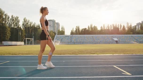 性感的年轻金发运动员在户外沿着跑道行走的照片 在阳光灿烂的早晨 女人在体育场跑步后放松了下来 高质量的4K镜头 — 图库视频影像