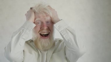 Aşırı mutlu, genç albino bir adamın, mutluluktan deliye döndüğü bir ortamda. Albinizmi olan yakışıklı bir adam saçlarını heyecanla savuruyor. Şaşırmış görünüyor. Yüksek kalite 4k görüntü