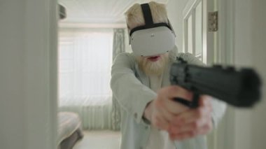 Büyük siyah oyuncak tabancalı albino adam evde VR kulaklıkla atış oyunu oynuyor. Beyaz iç dizaynı olan odaların bulanık arkaplanı. Dijital dünya. Yüksek kalite 4k görüntü