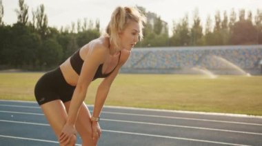 Stadyumda egzersiz yaptıktan sonra dinç, genç bir sarışın. Nefes alma egzersizleri. Kadın öne eğiliyor, dizlerinin üstüne çöküp temiz havayı soluyor. Yüksek kalite 4k görüntü