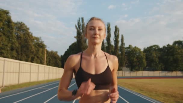 スポーティなブロンドの実行中のショット 汗びっしょりの体をした若い女性が晴れた日にスタジアムのランニングコースを走っている 健康的な生活 毎日のワークアウト 高品質4K映像 — ストック動画