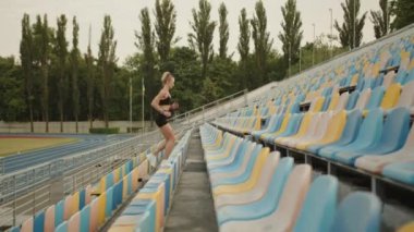 Sportif sarışının profil fotoğrafı üst katta stadyumda koşuyor. Stadyumun merdivenlerinde renkli koltuklarla egzersiz yapan bir kadın. Üst katta dışarıda koşuyor. Yüksek kalite 4k görüntü