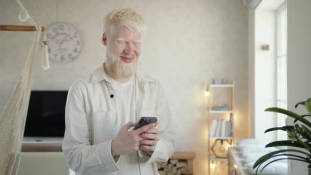 Hombre Albino Feliz Charlando Teléfono Inteligente Soñando Sonriendo Pie Sala — Vídeos de Stock