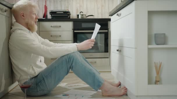 Młody Albinos Szaleje Rozrywając Kartkę Papieru Kawałki Siedząc Podłodze Kuchni — Wideo stockowe