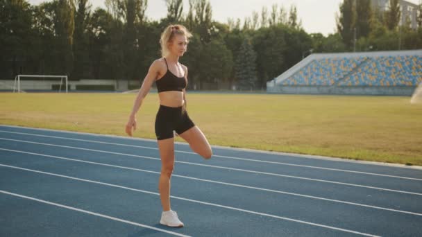 漂亮的金发姑娘在体育场跑步前做伸展腿的运动 女人在新鲜空气中在跑道上表演四重唱 高质量的4K镜头 — 图库视频影像