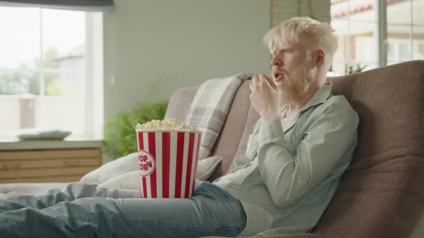Opgewonden Bebaarde Albino Man Zittend Bank Woonkamer Popcorn Etend Kijkend — Stockvideo