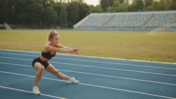 田径运动的金发姑娘在跑前热身 腿在室外伸展运动 身体汗流浃背的女人在体育场的跑道上表演侧泳 高质量的4K镜头 — 图库视频影像