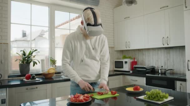自宅のモダンなキッチンのまな板にトマトを切るアルビノの男は 仮想現実の眼鏡をかけています デジタル世界 Vrメガネのアルビノ男が調理する 高品質4K映像 — ストック動画
