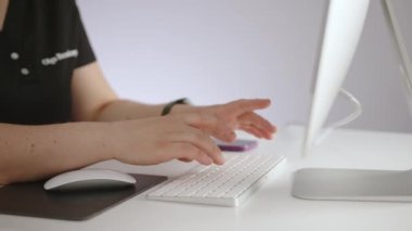 Sıhhiye üniformalı bir kadın rahat ofisinde bilgisayarda çalışıyor klinikteki masada oturuyor. Bilgisayarı ve cep telefonu olan düzgün bir masaüstü. Yüksek kalite 4k görüntü