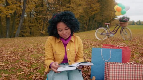 秋の公園でのカーリー ダーク ヘアカラーの女性のレジャータイム 本を読み ショッピングや自転車に乗って新鮮な空気をリラックス 高品質の4K映像 — ストック動画