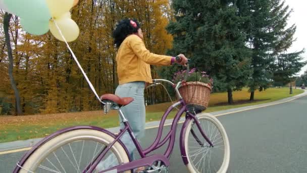 欢快的彩色女性漫步在荒无人烟的长路上 秋天的树上 抱着附有气球的自行车和鲜花的篮子 享受生活 高质量的4K镜头 — 图库视频影像