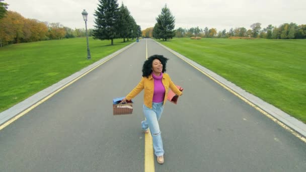 一个色彩艳丽的年轻女子形象 在两边都是绿绿的草坪 街灯和一排排的秋树的道路上愉快地购物之后 高质量的4K镜头 — 图库视频影像